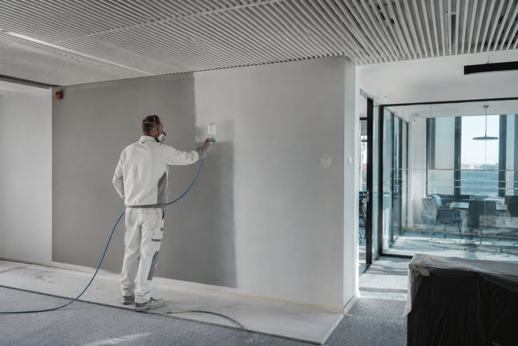 Schilder die bezig is met het uitvoeren van spuitwerk in een kantoorpand